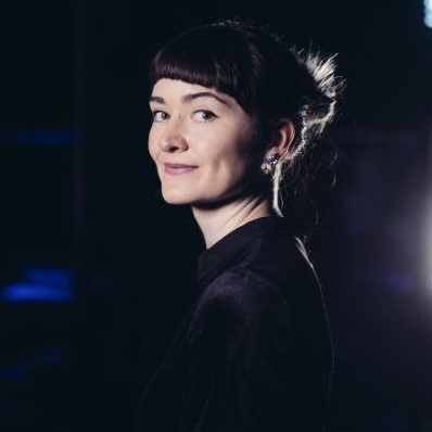 Elaine Burke wearing a black top standing with stage lights in the background